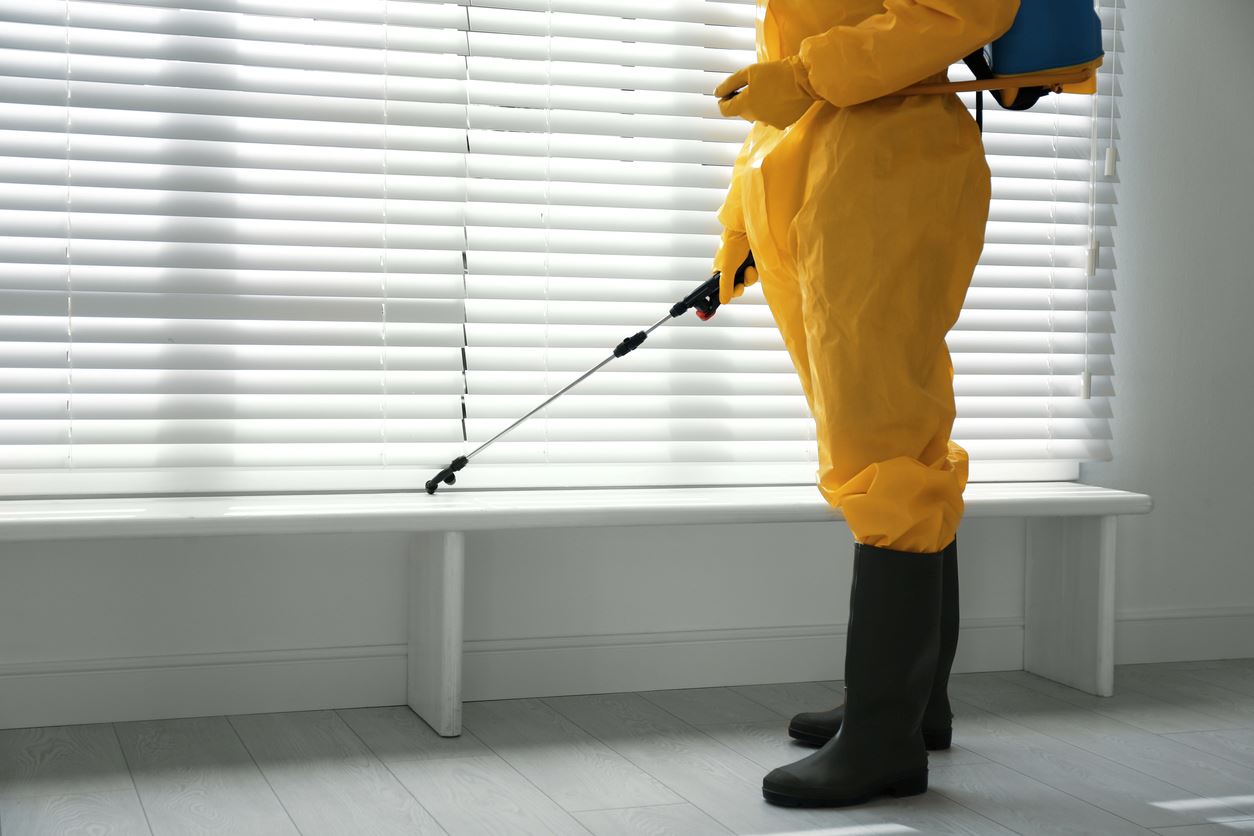 A pest tech in a yellow covering sprays pesticides inside a home