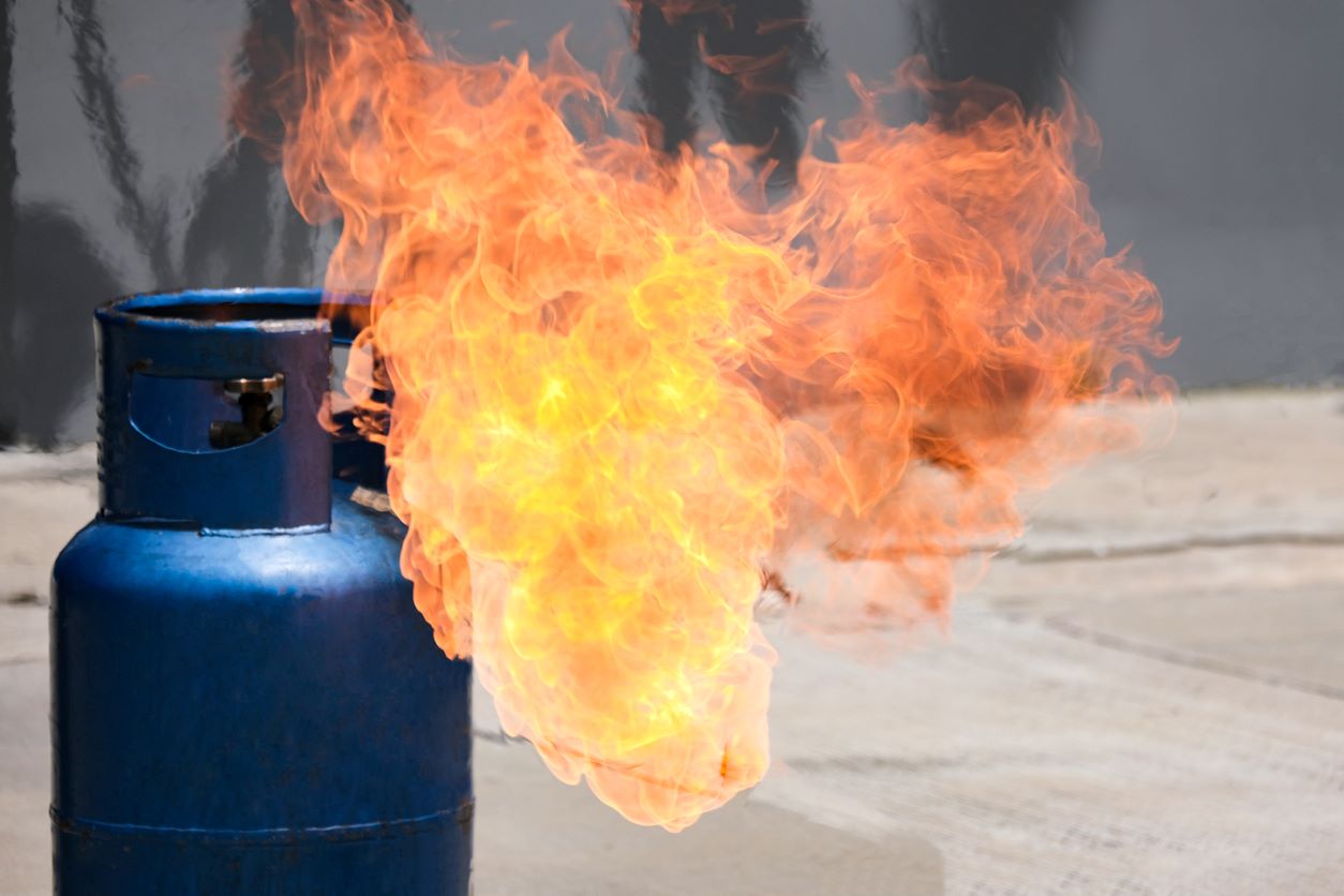A blue propane tank sitting on the concrete releases a burst of fire.