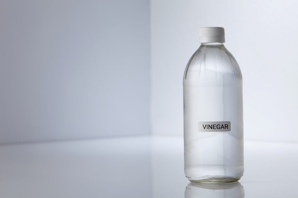 A small, clear plastic bottle that reads “vinegar” in front of a white background