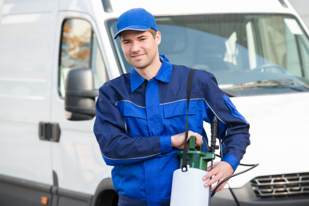 Pest control technician carrying pesticide with truck parked in the background.