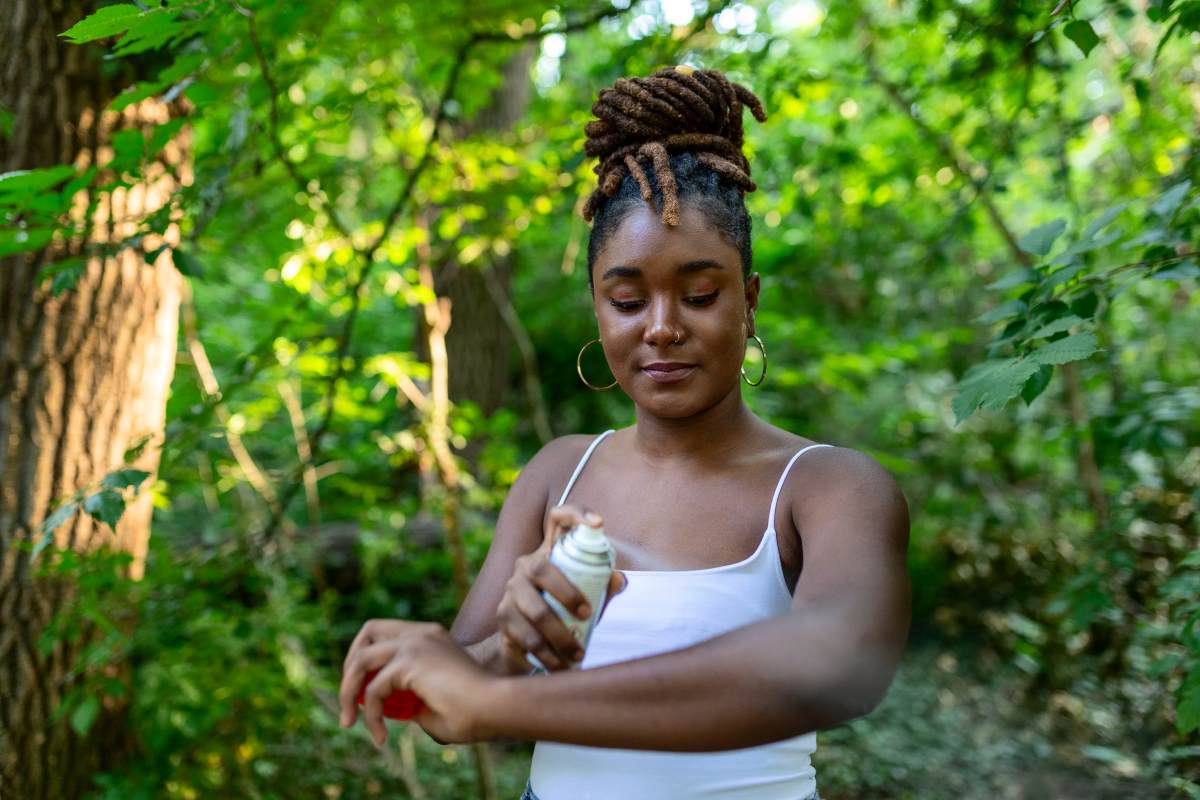 Woman applying mosquito repellent spray while in the woods. 
