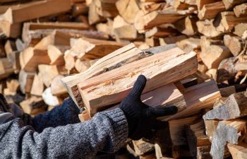 Man taking dry split firewood from stack for heating house